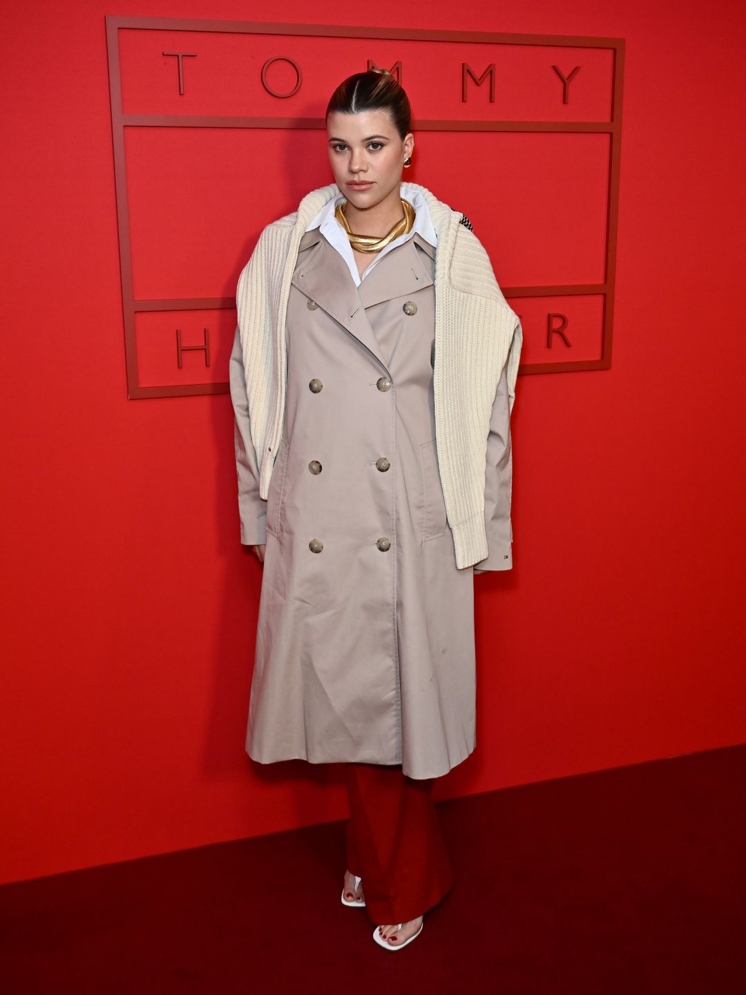 Sofia Richie attends the Tommy Hilfiger show during New York Fashion Week wearing a trench coat and red trousers 