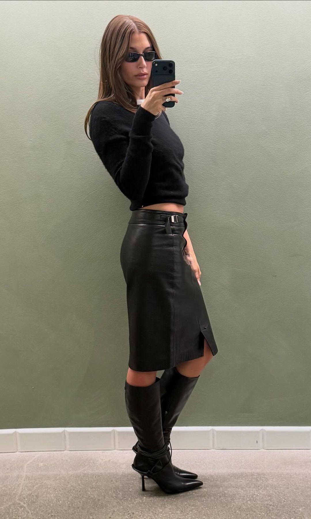 Hailey Bieber poses in a black leather skirt and knee-high boots