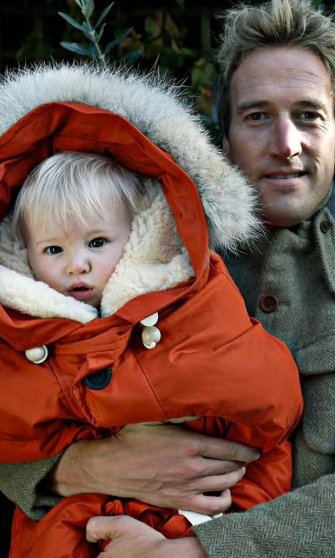 Ben Fogle tenant un bébé dans une parka orange