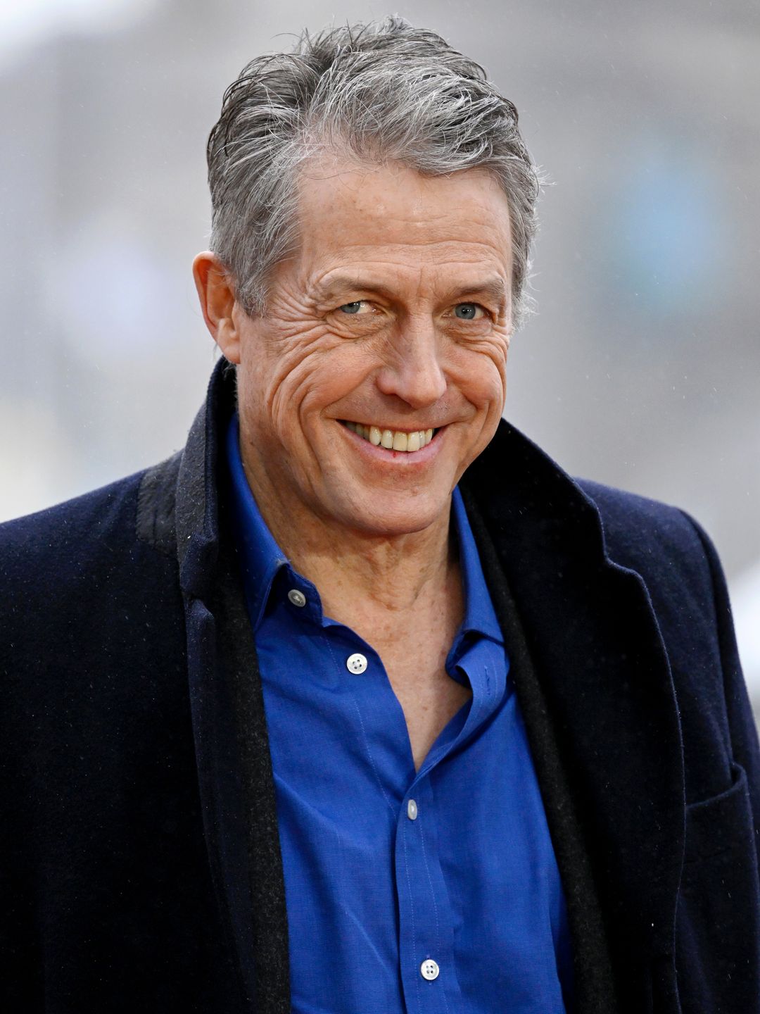 Hugh Grant in a black jacket and blue shirt