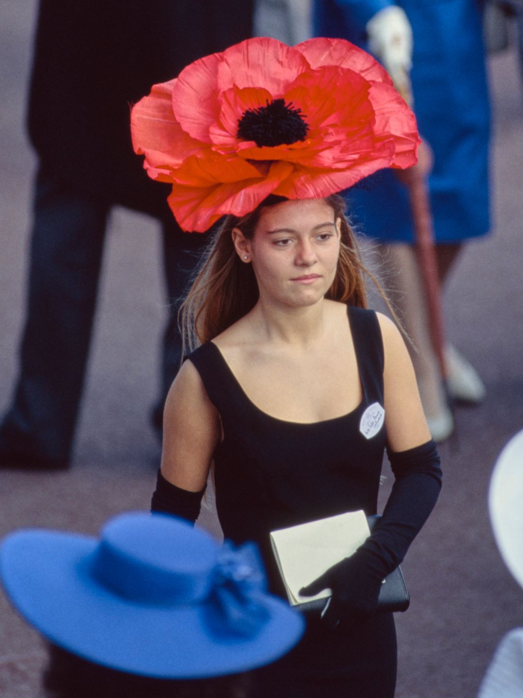 Uma participante de corrida usando um vestido preto, luvas de noite pretas e um chapéu vermelho de papoula no primeiro dia do Royal Ascot, 19 de junho de 1990.
