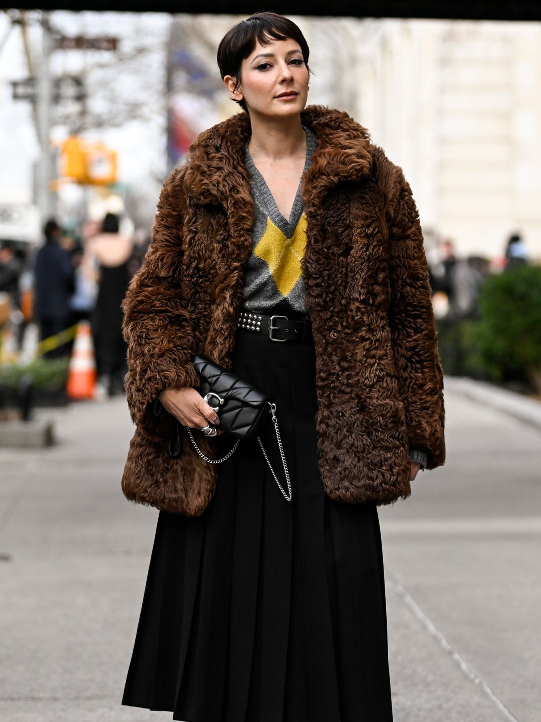 Alyssa Coscarelli is seen wearing a faux brown fur coat, yellow and gray sweater, black skirt and black boots with black Coach purse outside the Coach show 