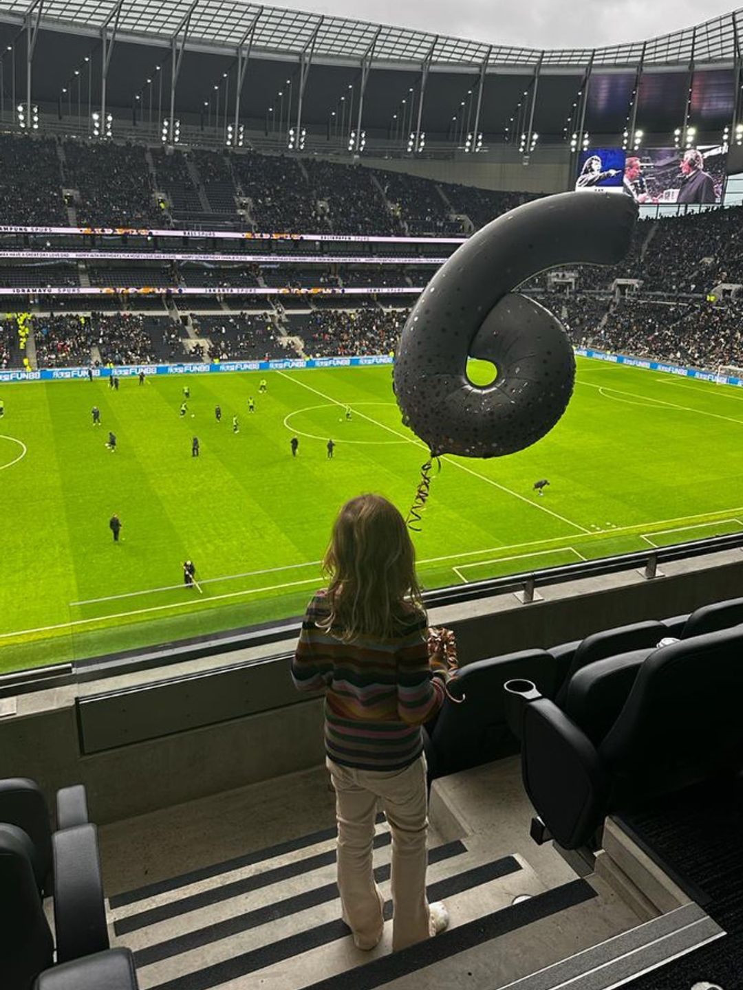 A young girl watching a football match with a '6' balloon