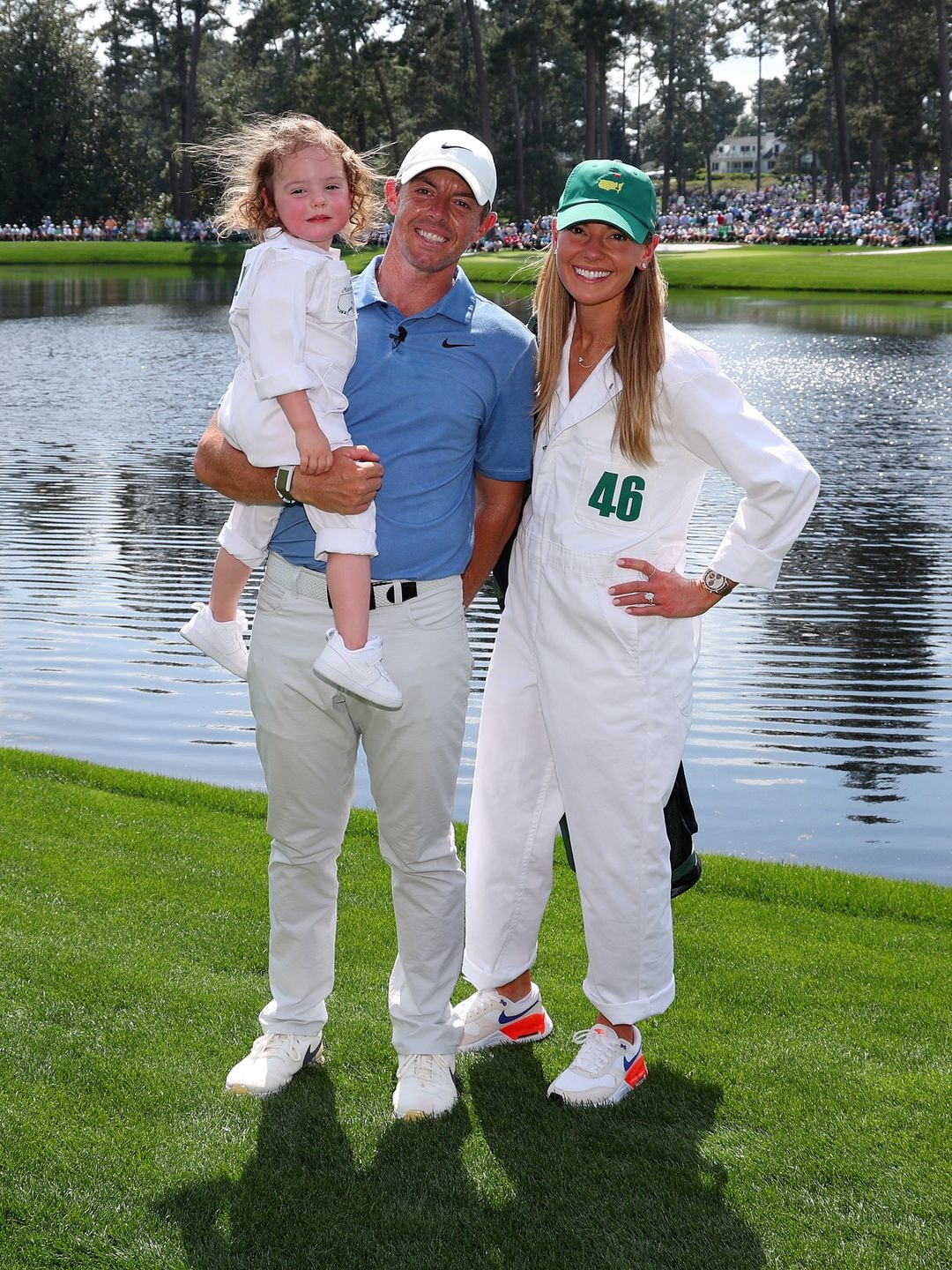 Rory McIlroy with his wife Erica Stoll and daughter Poppy McIlroy stood smiling on a golf course a lake behind them