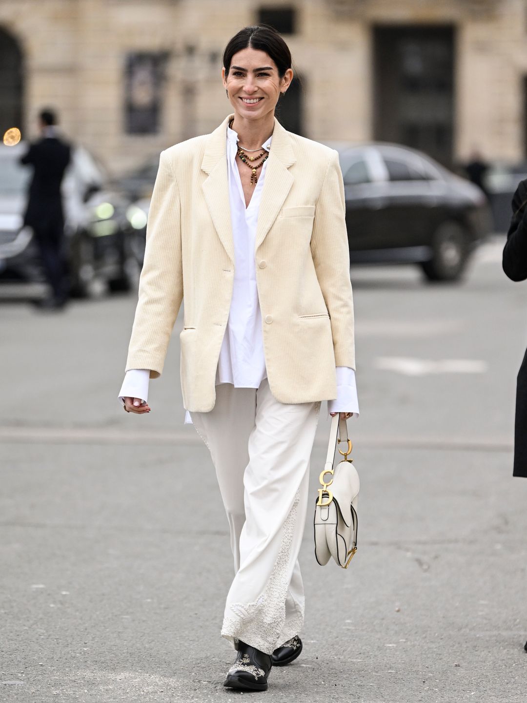 Deborah Reyner Sebag is seen wearing a cream jacket, white button down shirt, white pants, black shoes and black sunglasses outside the Dior show