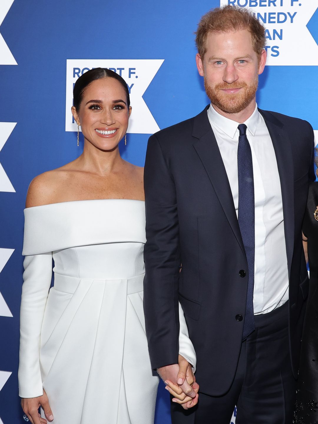Meghan Markle in a white dress standing with Prince Harry in a suit