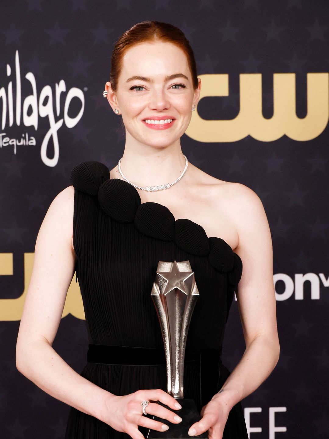 Emma Stone smiling in a black dress with her Critics' Choice Award 