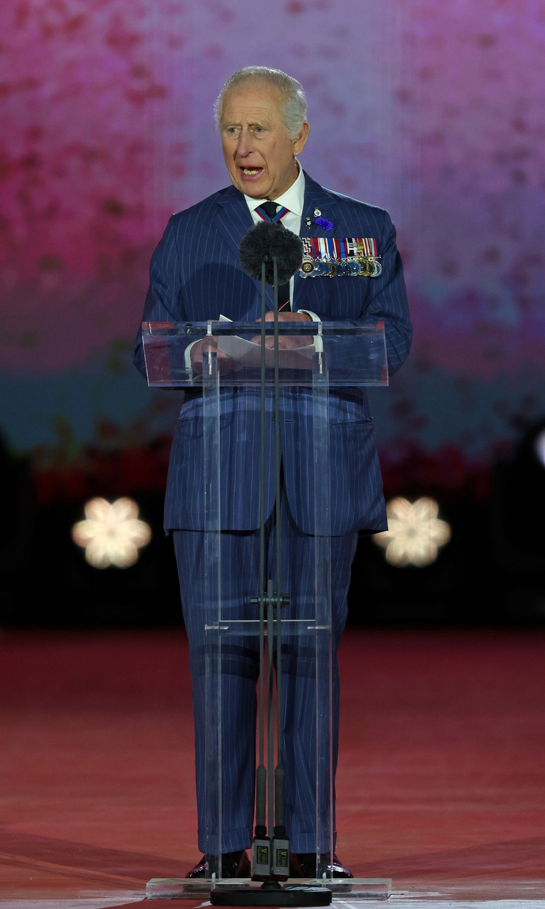 King Charles giving a speech in a blue suit with military medals