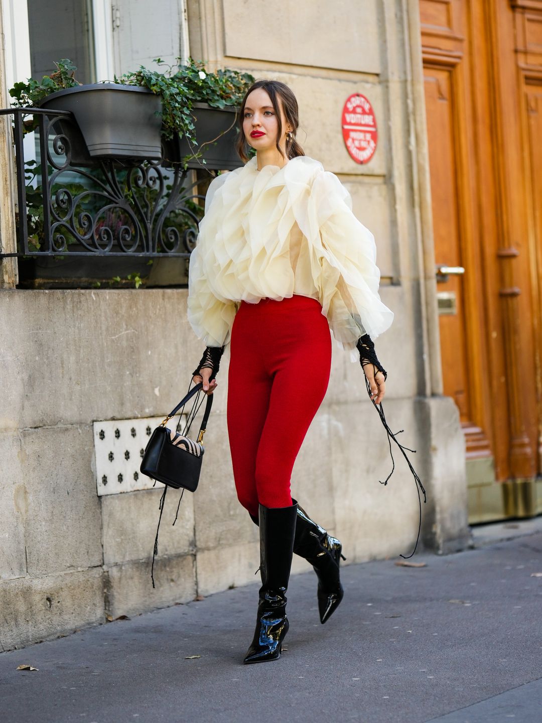 A Fashion Week guest wears bright red leggings with a cream ruffle blouse 