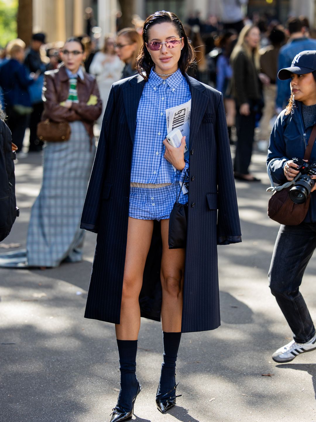 A fashion show guest wears navy striped coat, blue striped shorts, buttoned shirt outside Miu Miu during Womenswear Spring/Summer 2025 as part of  Paris Fashion Week