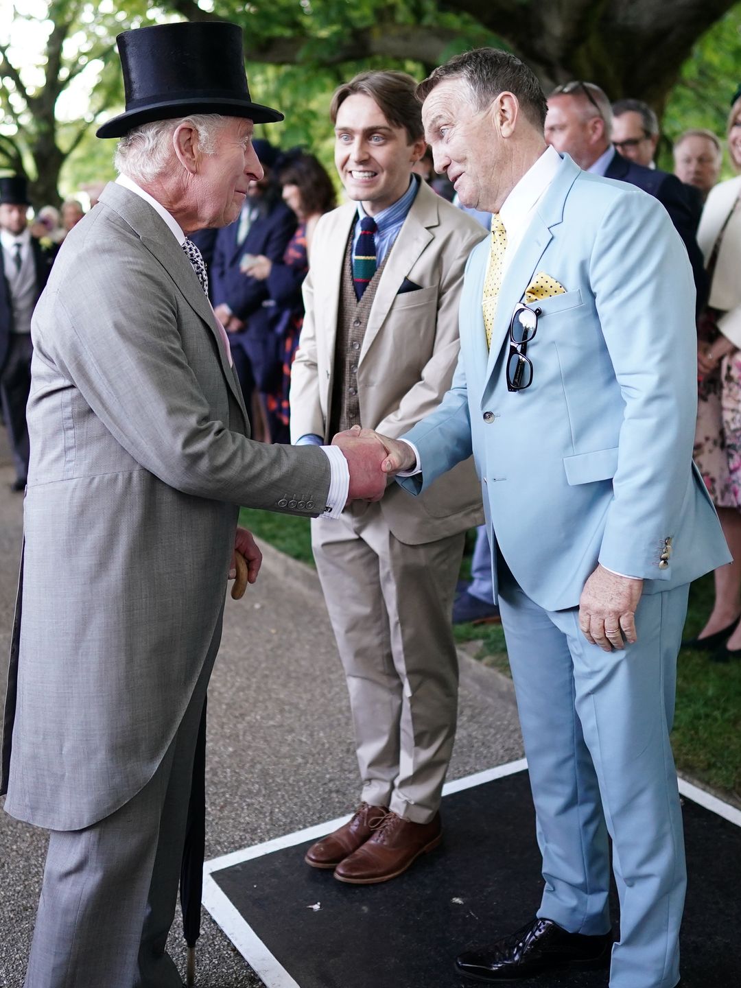 Bradley Walsh shaking hands with King Charles; Barney Walsh stands beside them