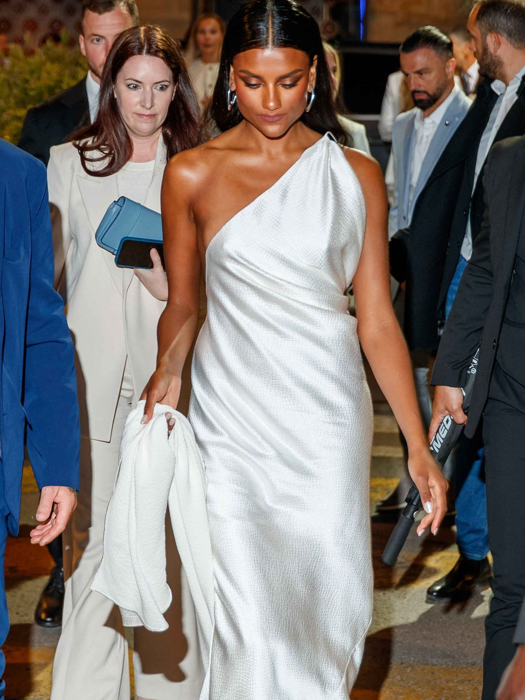 Simone Ashley holding the bottom of her white dress as she walks