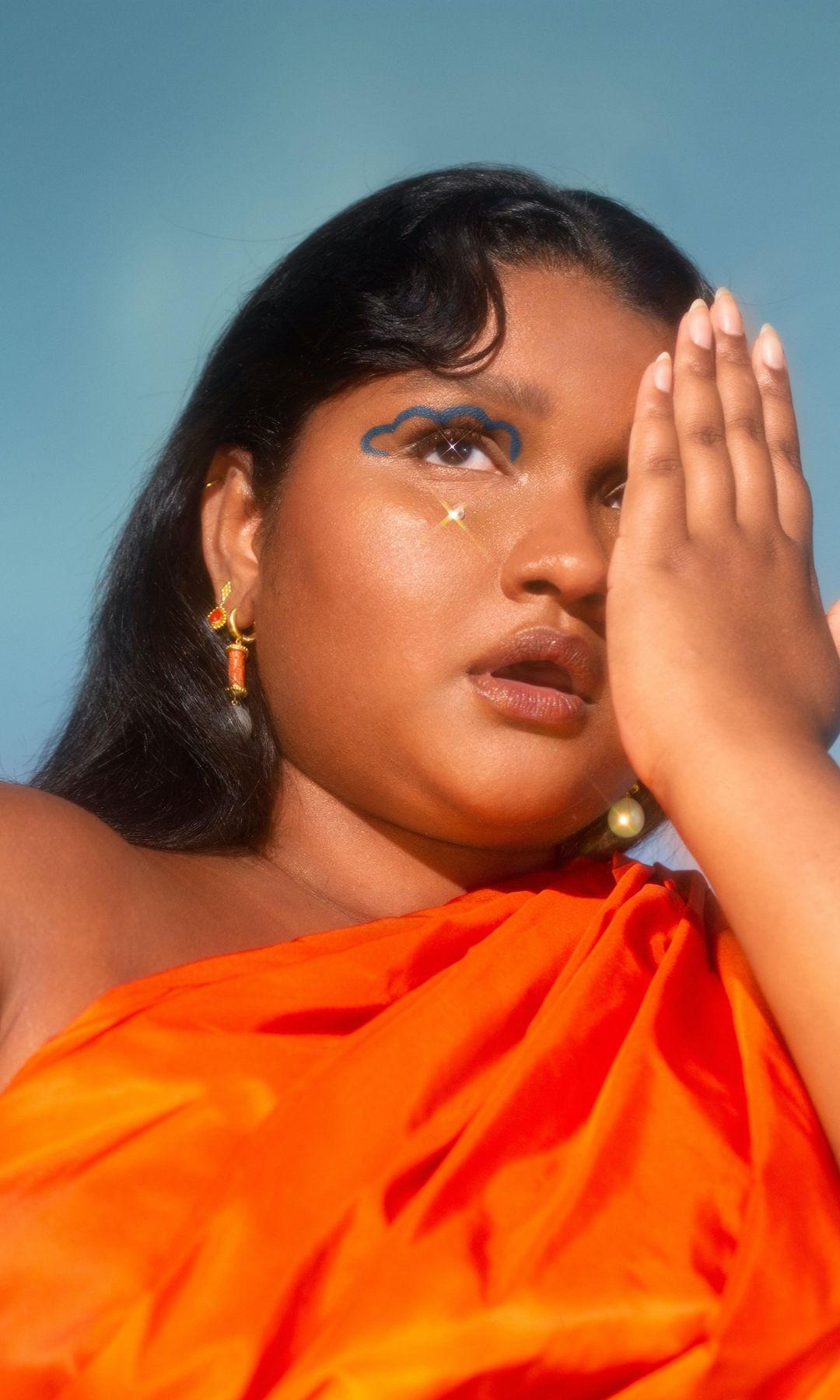 a woman in orange dress with one hand covering her eye 