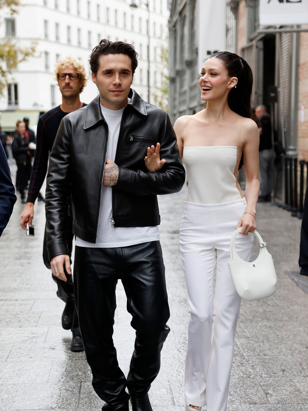 Brooklyn Beckham wears white t-shirt, black CourrÃ¨ges leather jacket, matching pants, black boots, and Nicola Peltz wears white jumpsuit with sheer details, white CourrÃ¨ges bag, outside CourrÃ¨ges,  during Womenswear Spring/Summer 2025 as part of  Paris Fashion Week on September 25, 2024 in Paris, France. (Photo by Claudio Lavenia/Getty Images)