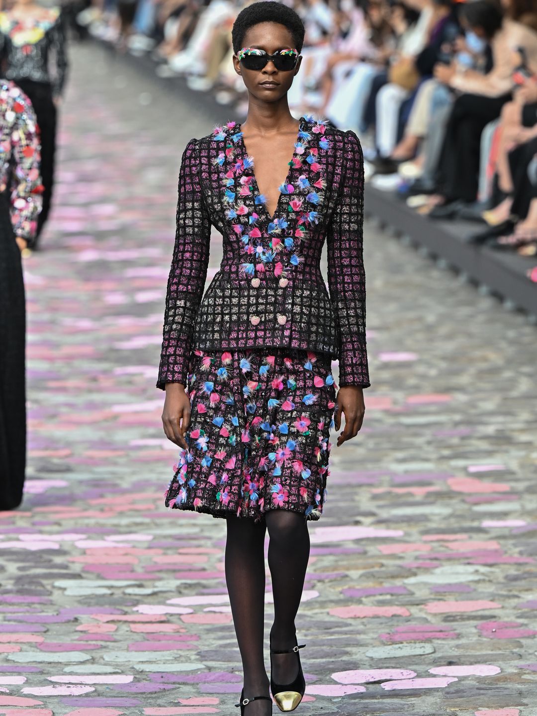 Chanel model wearing tweed jacket and skirt with blue and pink accents 