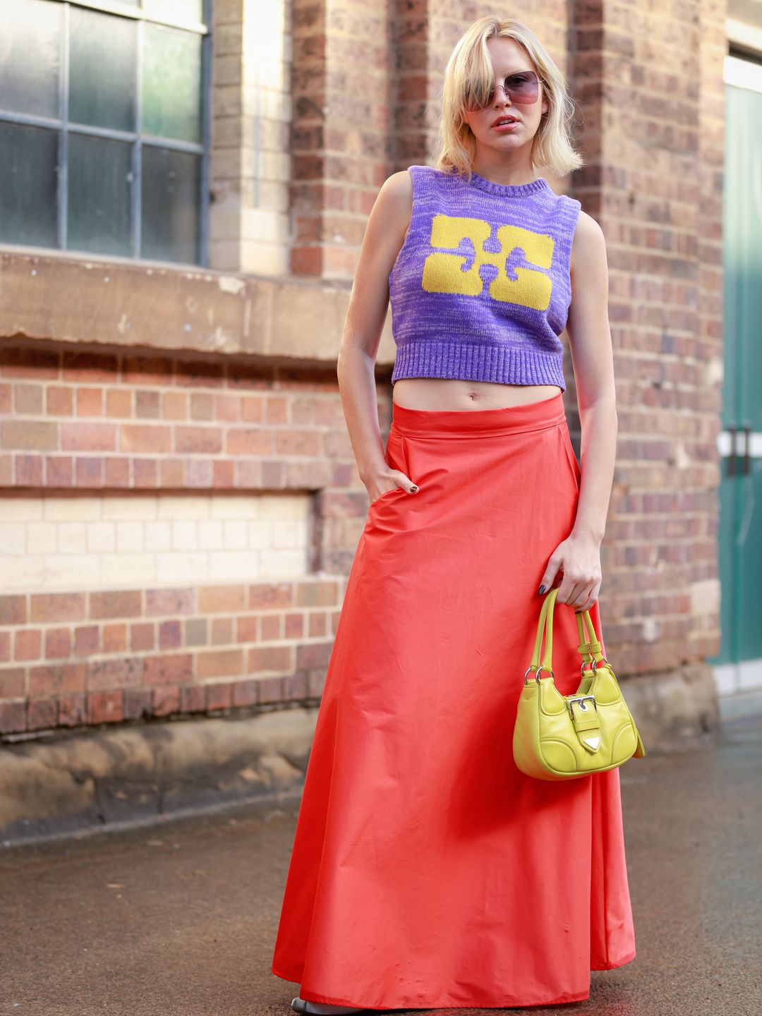 Violet Grace Atkinson wears a purple knitted vest with a red skirt and an acid green buckle bag 