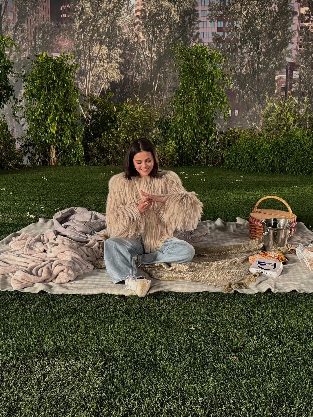 Selena Gomez shares a photo of herself sitting on a picnic blanket in jeans and a fluffy jacket after saying yes to Benny Blanco's proposal