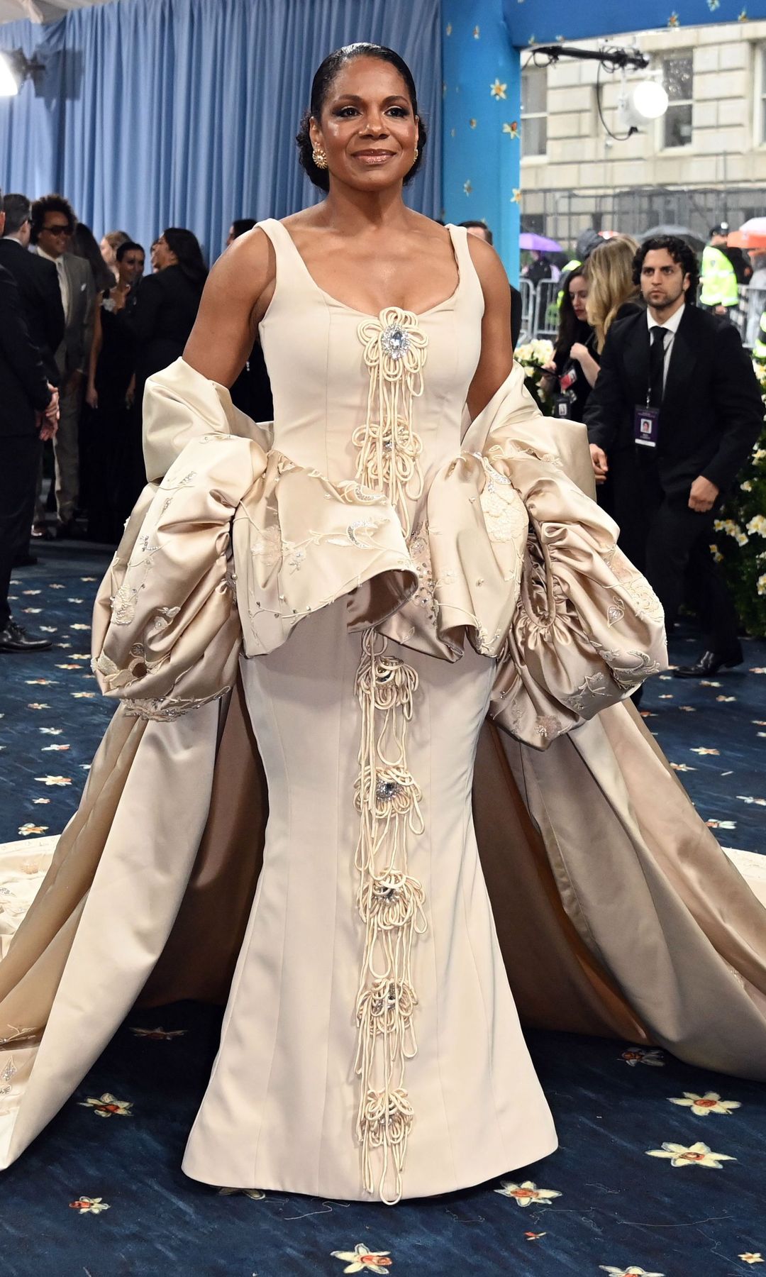 Audra McDonald wears a cream maxi dress with matching jacket with train and puff sleeves