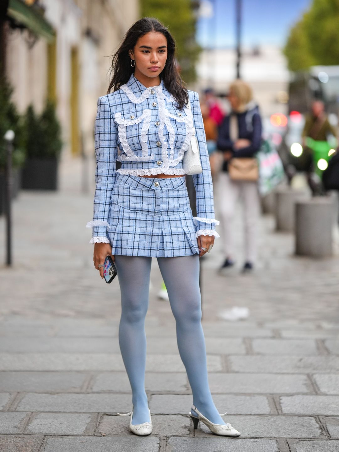 A Fashion Week guest wears a plaid skirt with a matching frilly jacket and dusty blue tights 