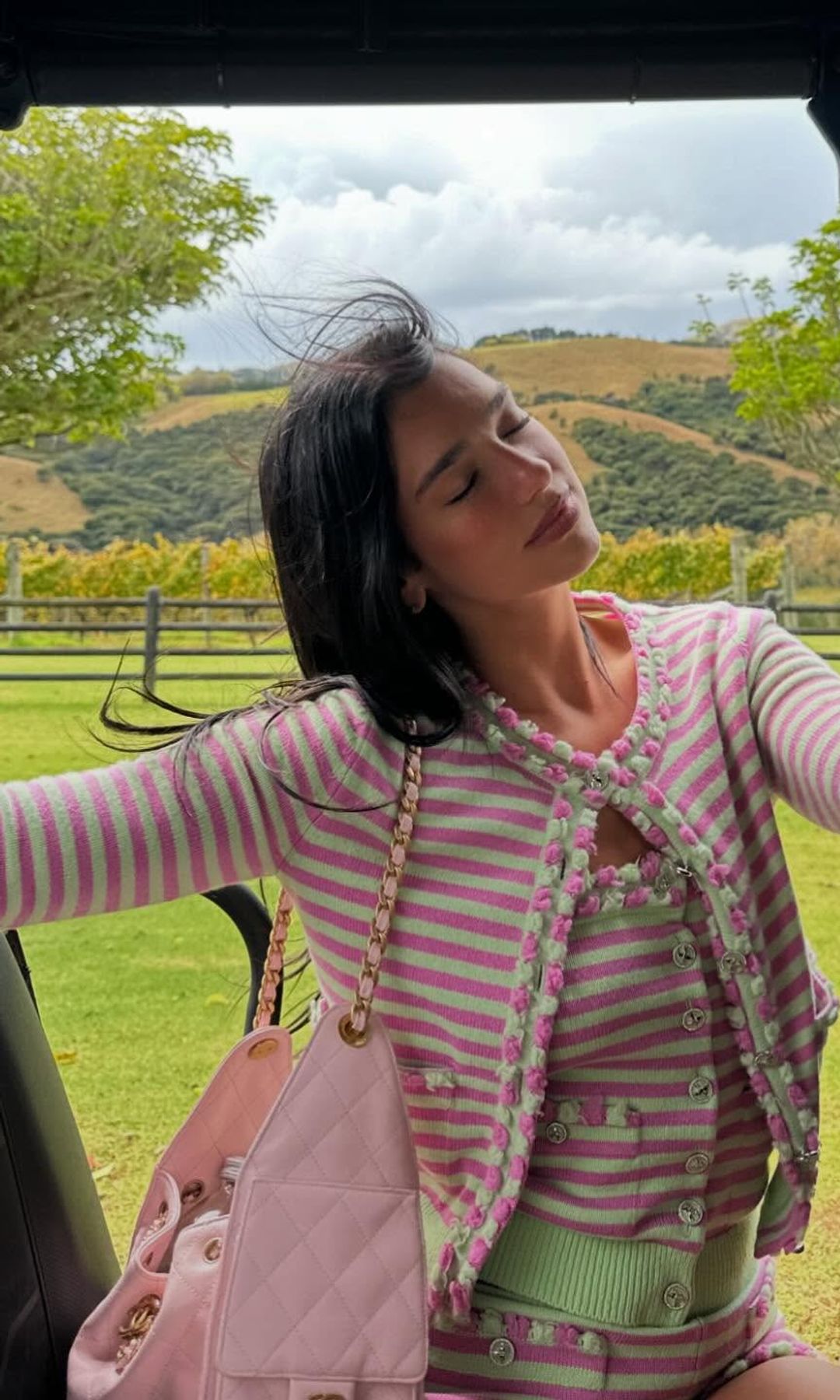 Dua Lipa poses in the back of a golf cart wearing a pink and green striped Chanel cardigan and mini short set