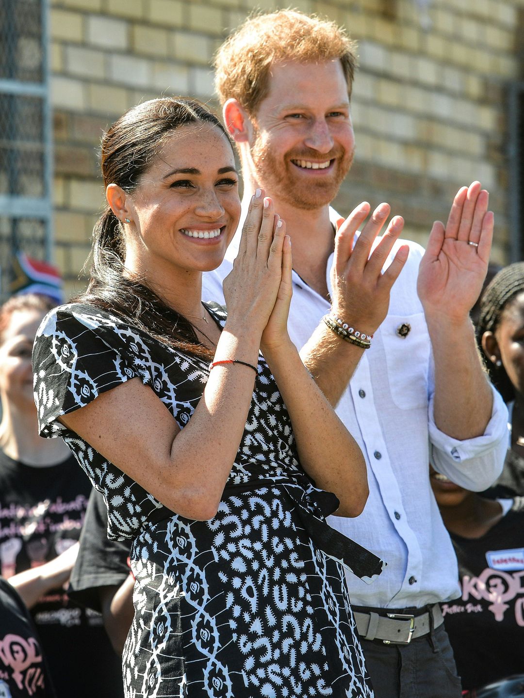Prince Harry and Meghan laughing and clapping at an event