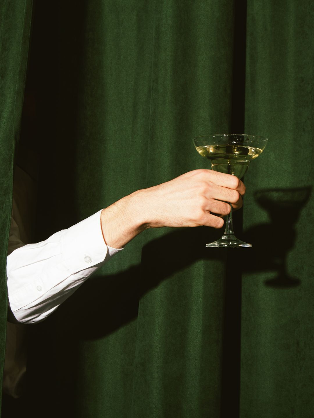 Hand with a martini glass sticks out from the green curtains