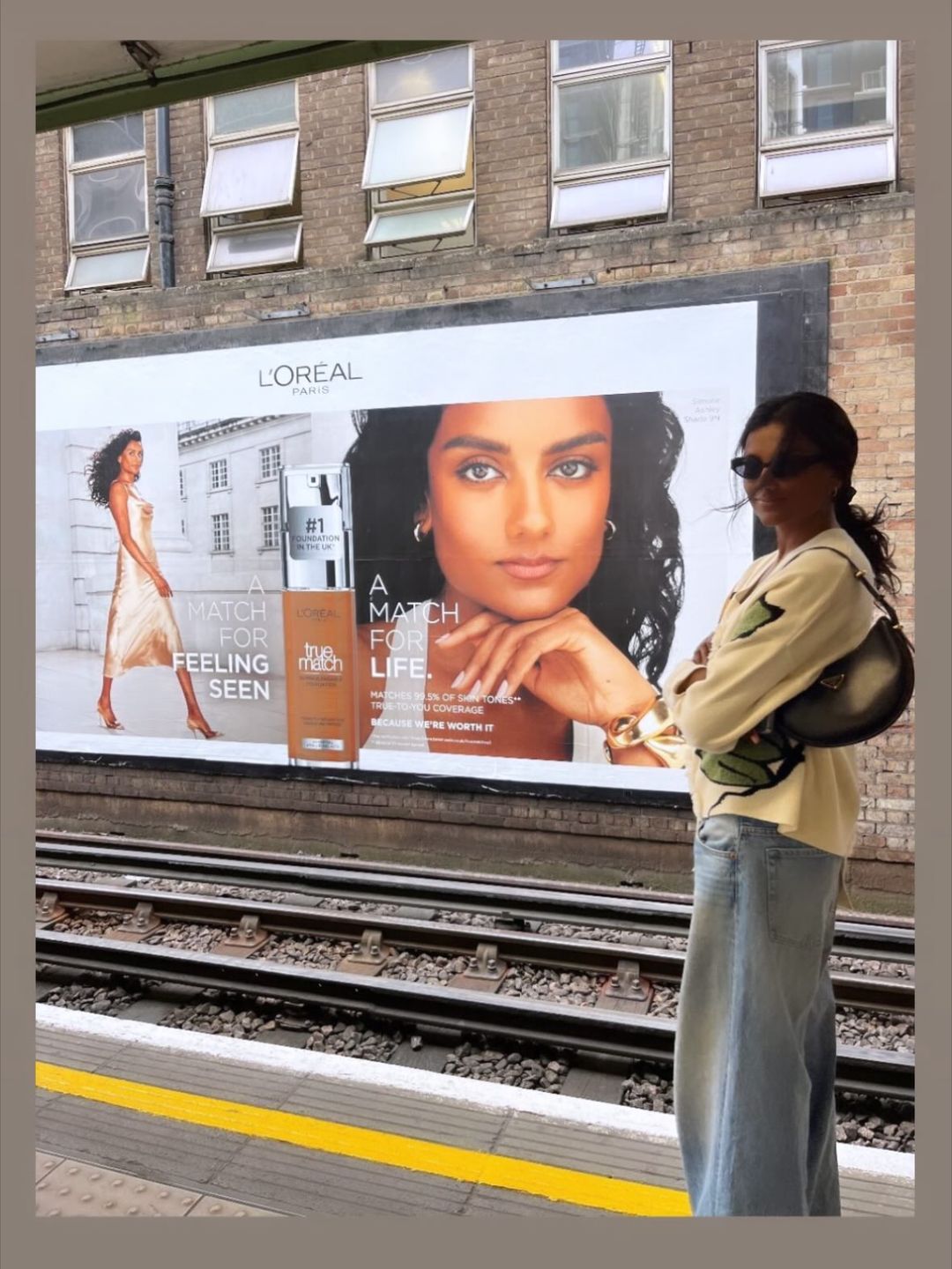 Simone Ashley poses in jeans and a sweatshirt infront of a Billboard