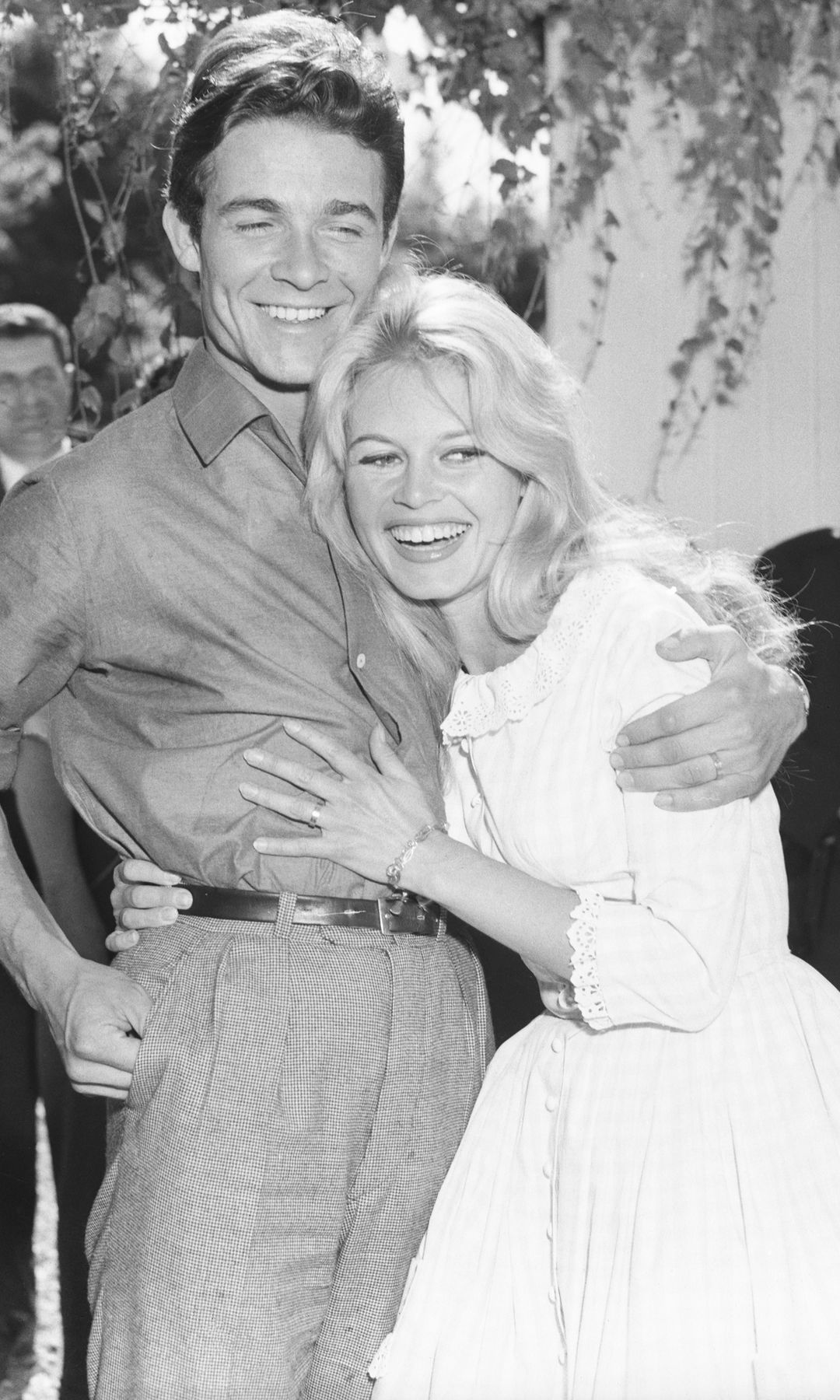 Brigitte Bardot And Jacques Charrier embrace at their wedding. Jacques wears a shirt and tie and Brigitte wears a high necked long dress in a gingham pattern.