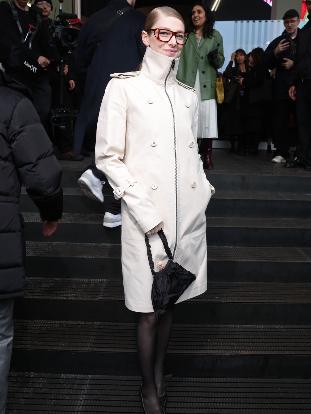 Hunter Schafer is seen arriving at the Prada fashion show in a zip-up trench coat, tights and heels