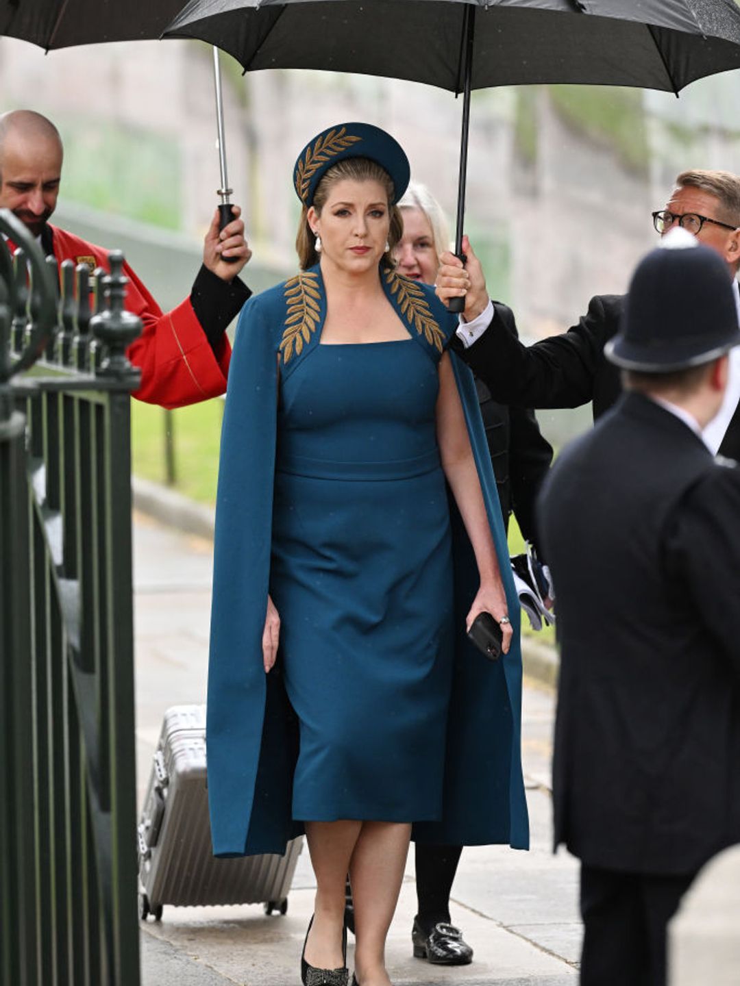 Penny wearing a teal cape dress embroidered with the golden fern motif of the Privy Council