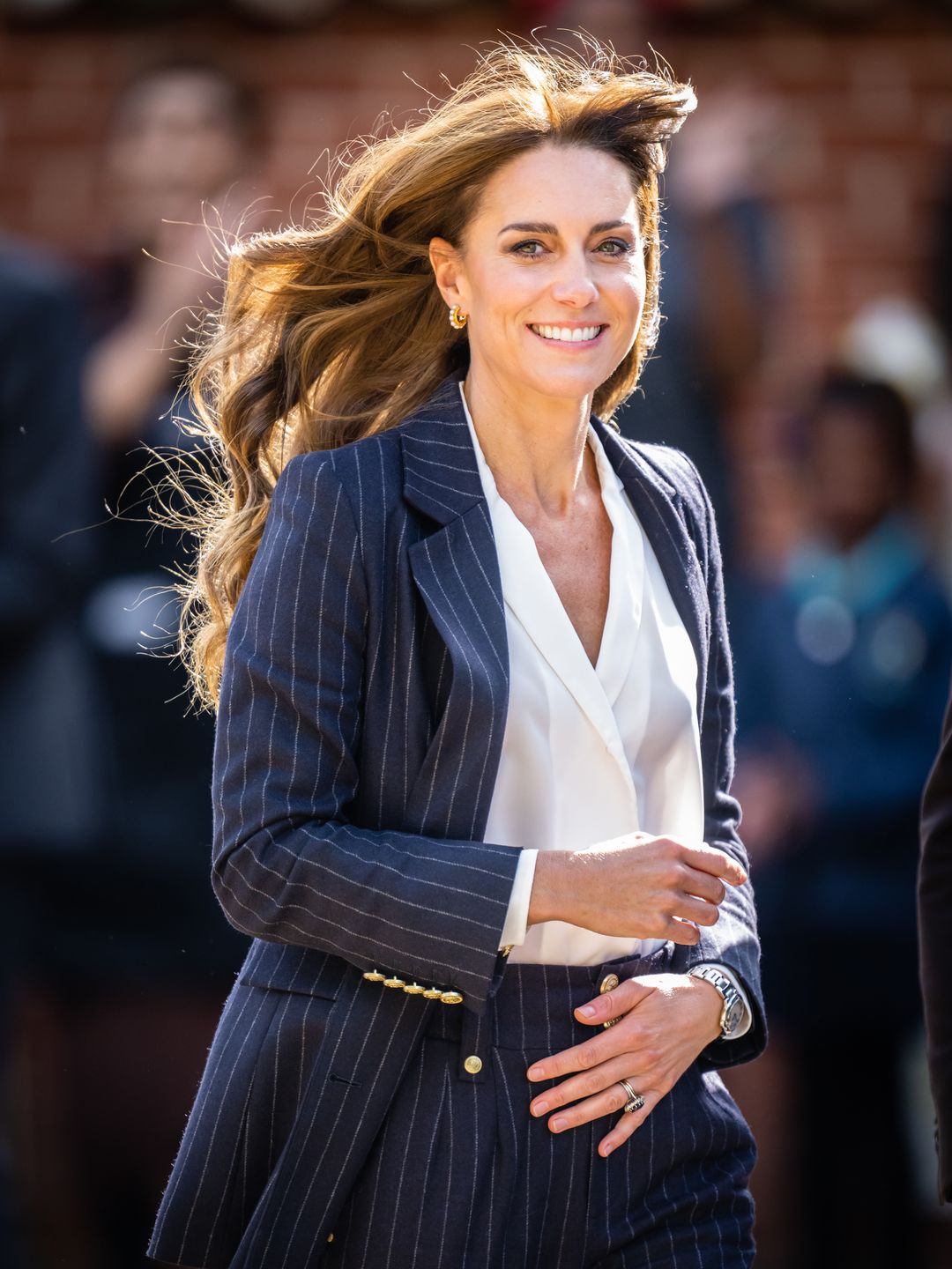 Kate Middleton wearing a blue navy pinstripe blazer, white shirt and matching pinstripe trousers in Cardiff. She has paired the look with gold jewellery and waves in her hair.  