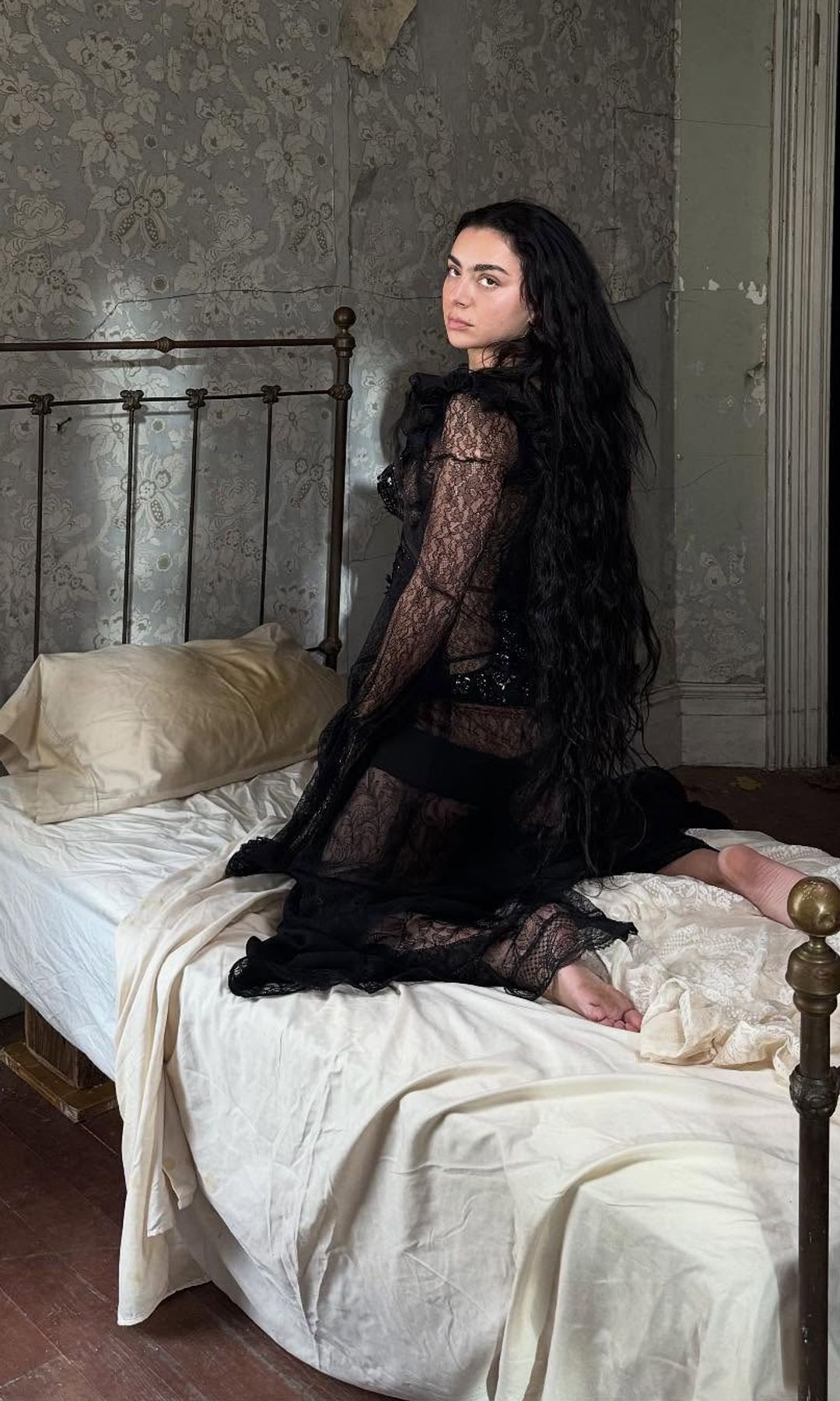 Charli XCX poses in a black dress on a bed 