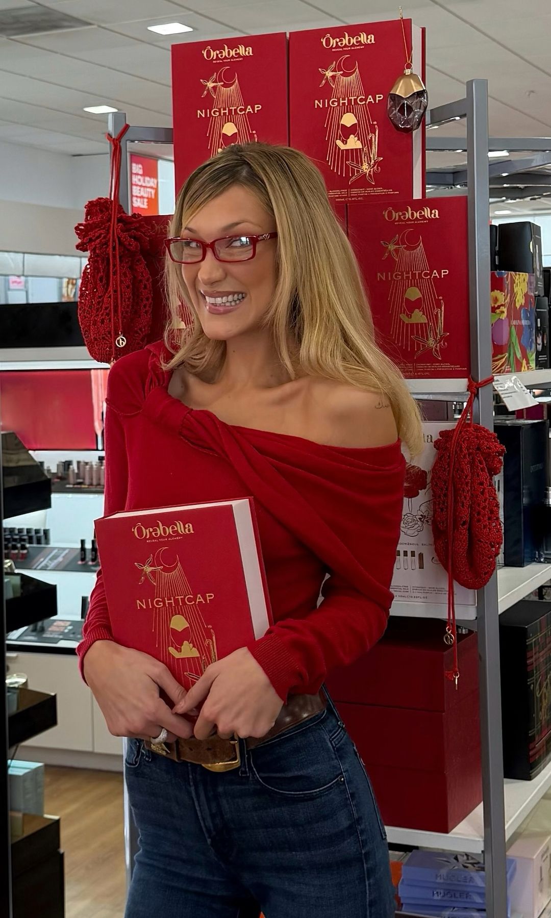 Bella Hadid poses in jeans and a red top at Ulta Beauty