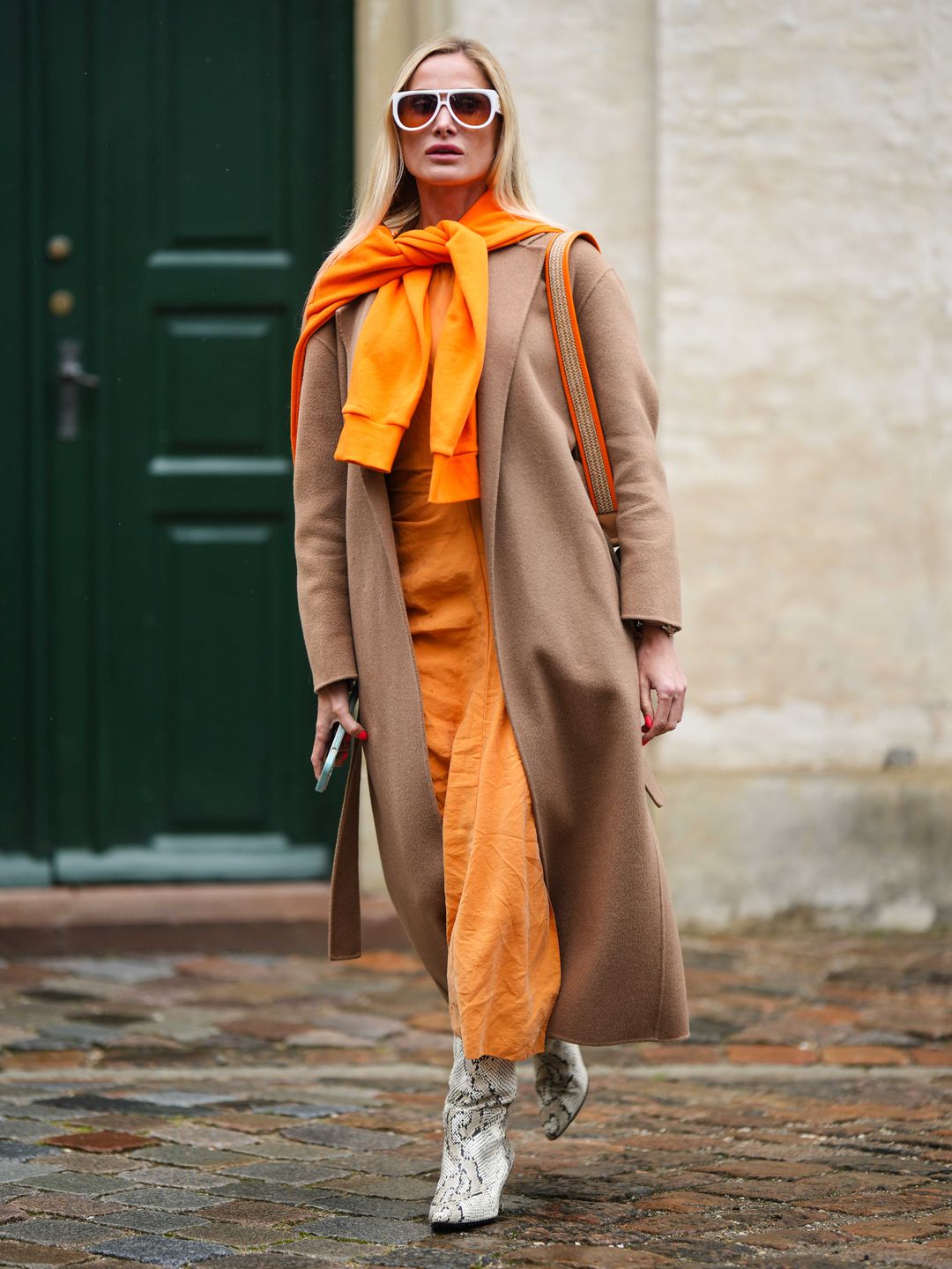 Fashion Week guest wearing a camel coat over an orange outfit 