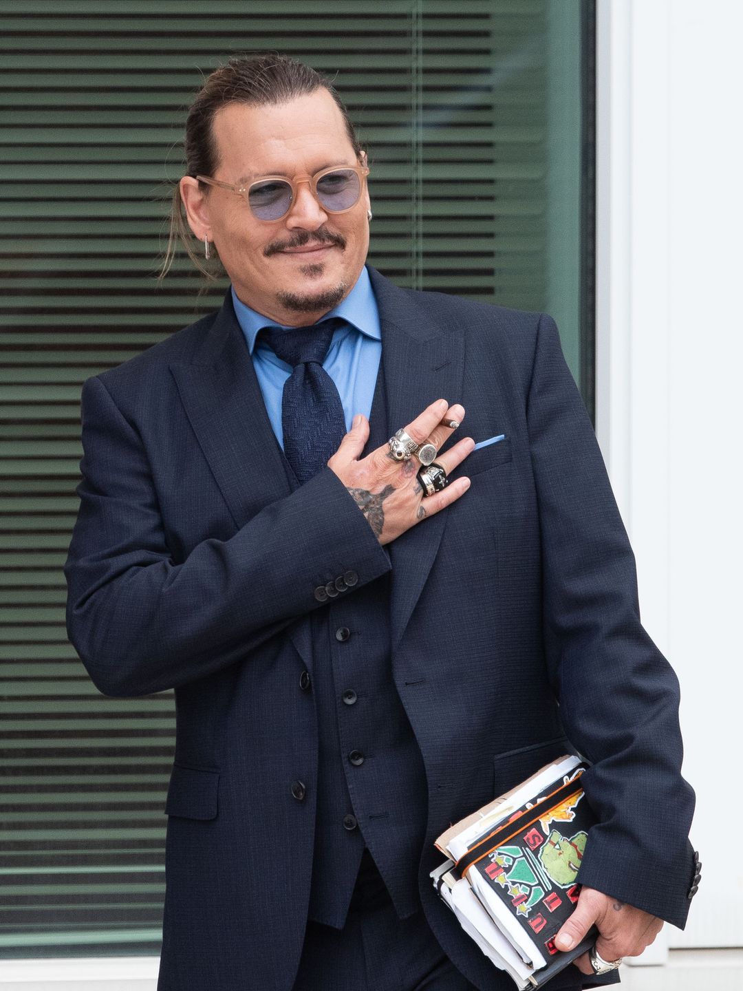Johnny Depp looking over to the right, he is carrying some papers and wearing sunglasses