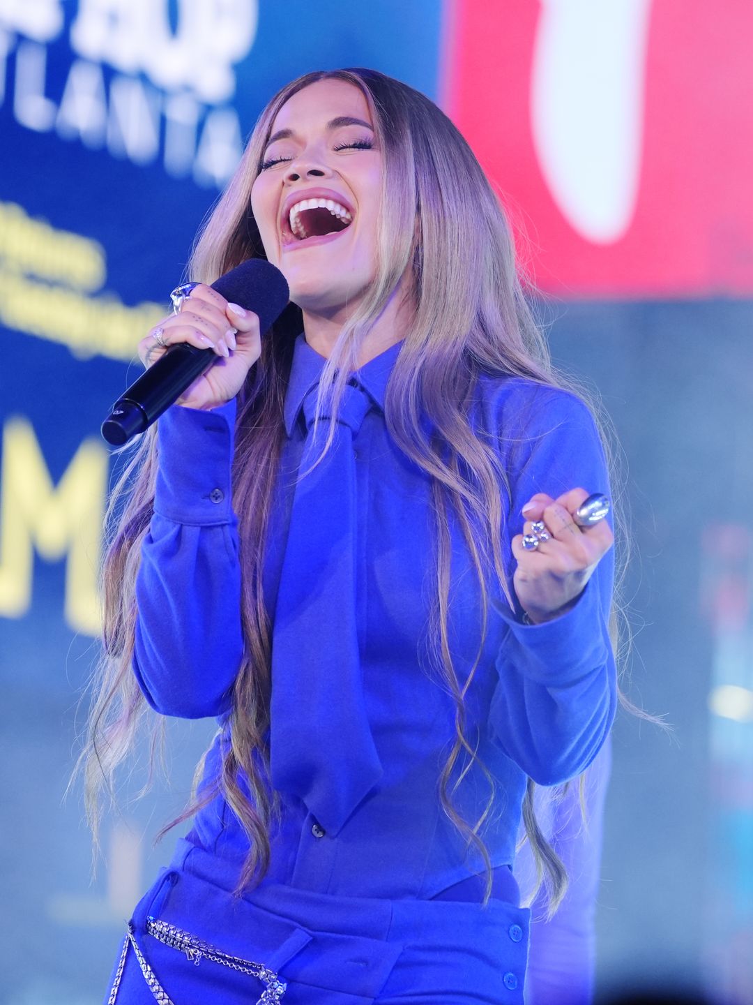 Rita Ora wears a purple shirt, tie and trousers while singing into a microphone for the New Year's Eve celebrations in Times Square, New York