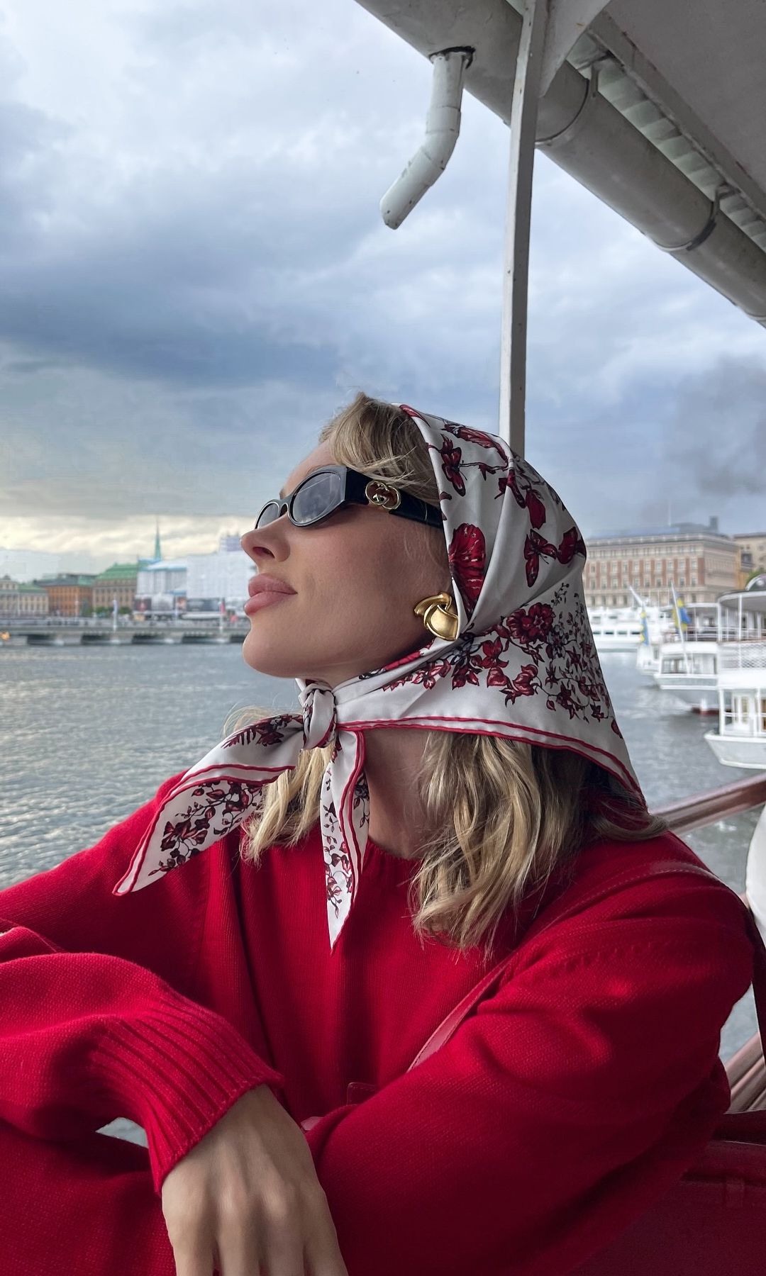 Elsa Hosk poses on a boat wearing a red jumper and headscarf