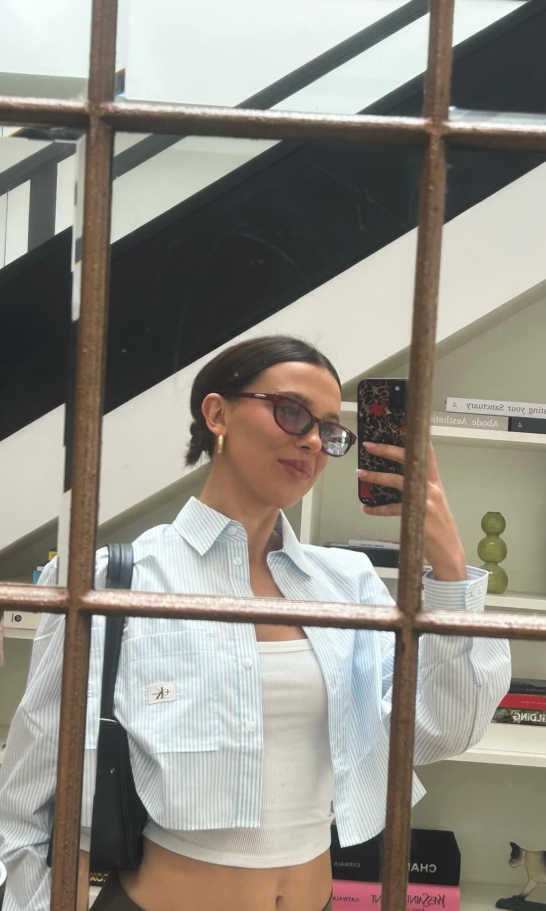 Millie Bobby Brown poses for a mirror selfie at home in a stripe crop shirt and ribbed tank top