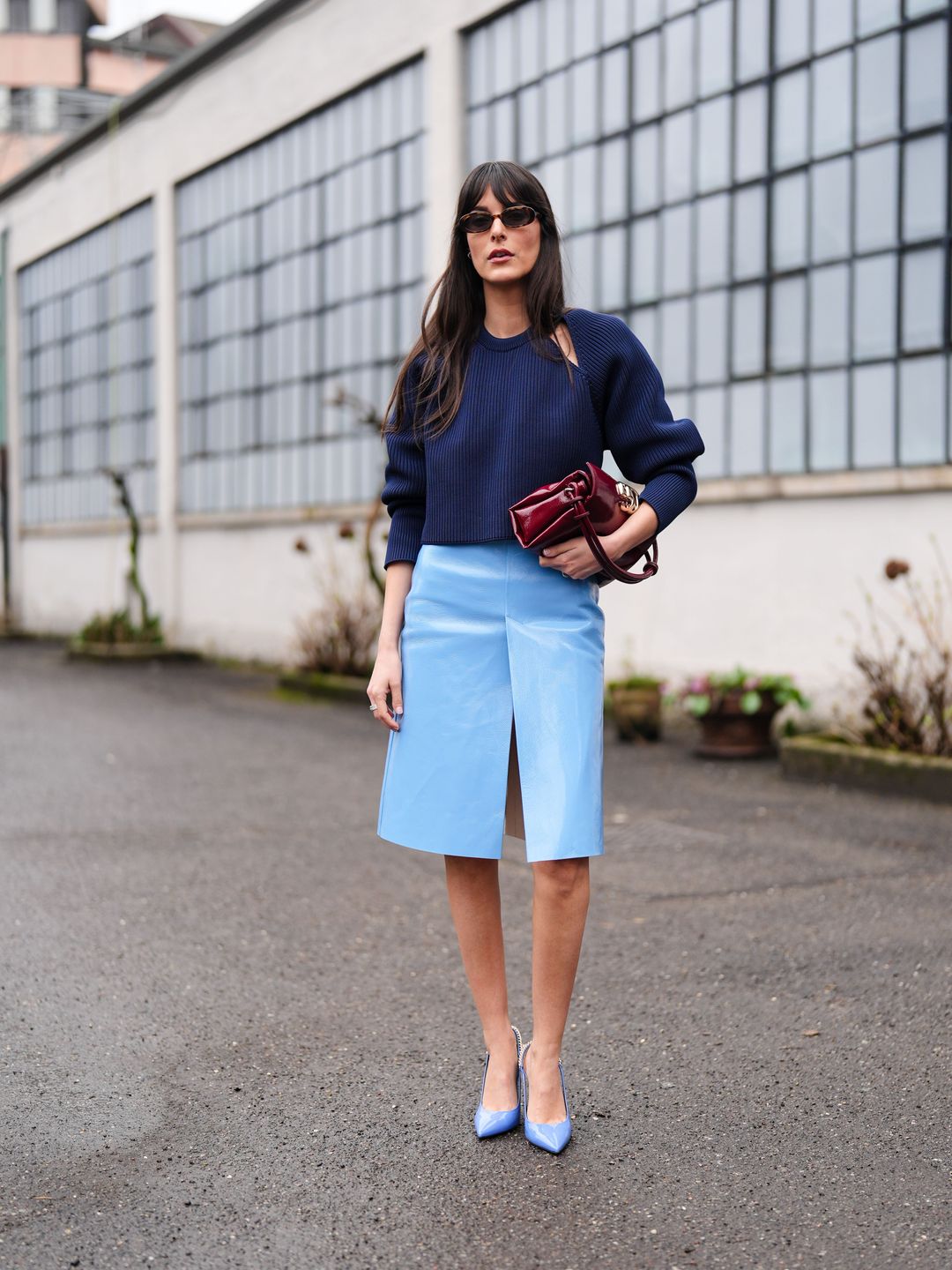 Leia Sfez wears a dark blue ribbed knitted wool pullover with puff sleeves, a burgundy leather bag, a pastel pale slit skirt in leather , pointed shoes , outside Gucci