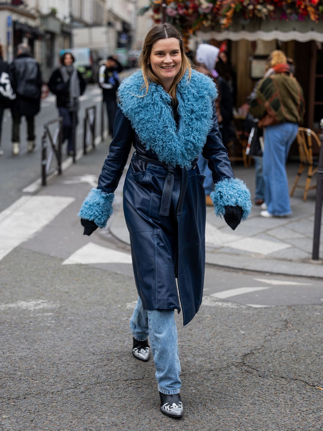 A Fashion Week guest wears a navy belted coat with jeans and two-tone cowboy boots 