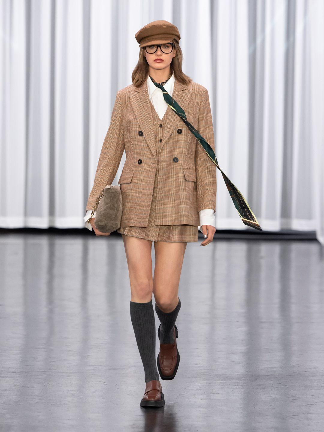A Model at Marc Cain wears a matching skirt and blazer with knee high socks and brown loafer shoes