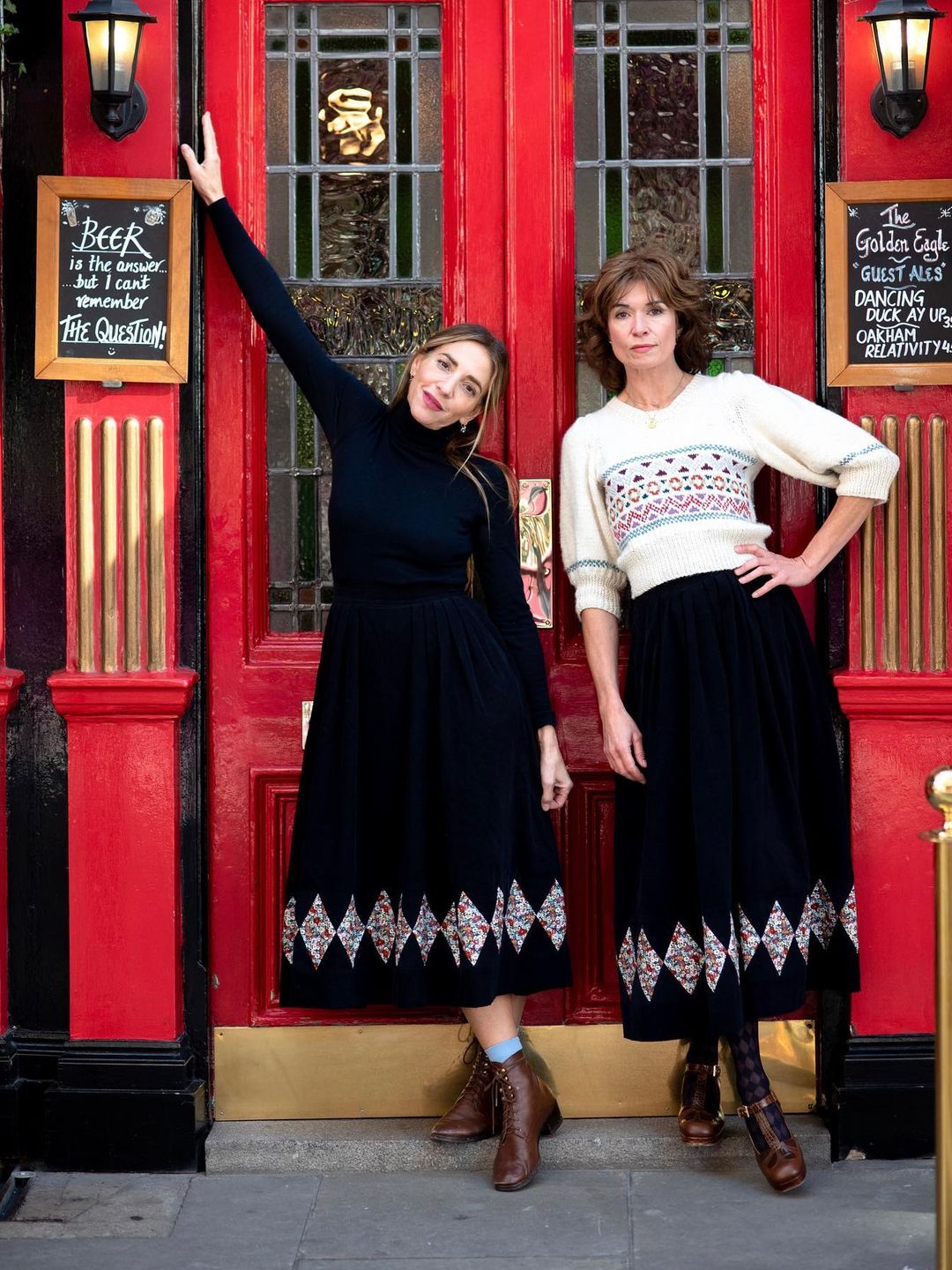 Tania and Clara from O Pioneers posing in front of a red set of doors.