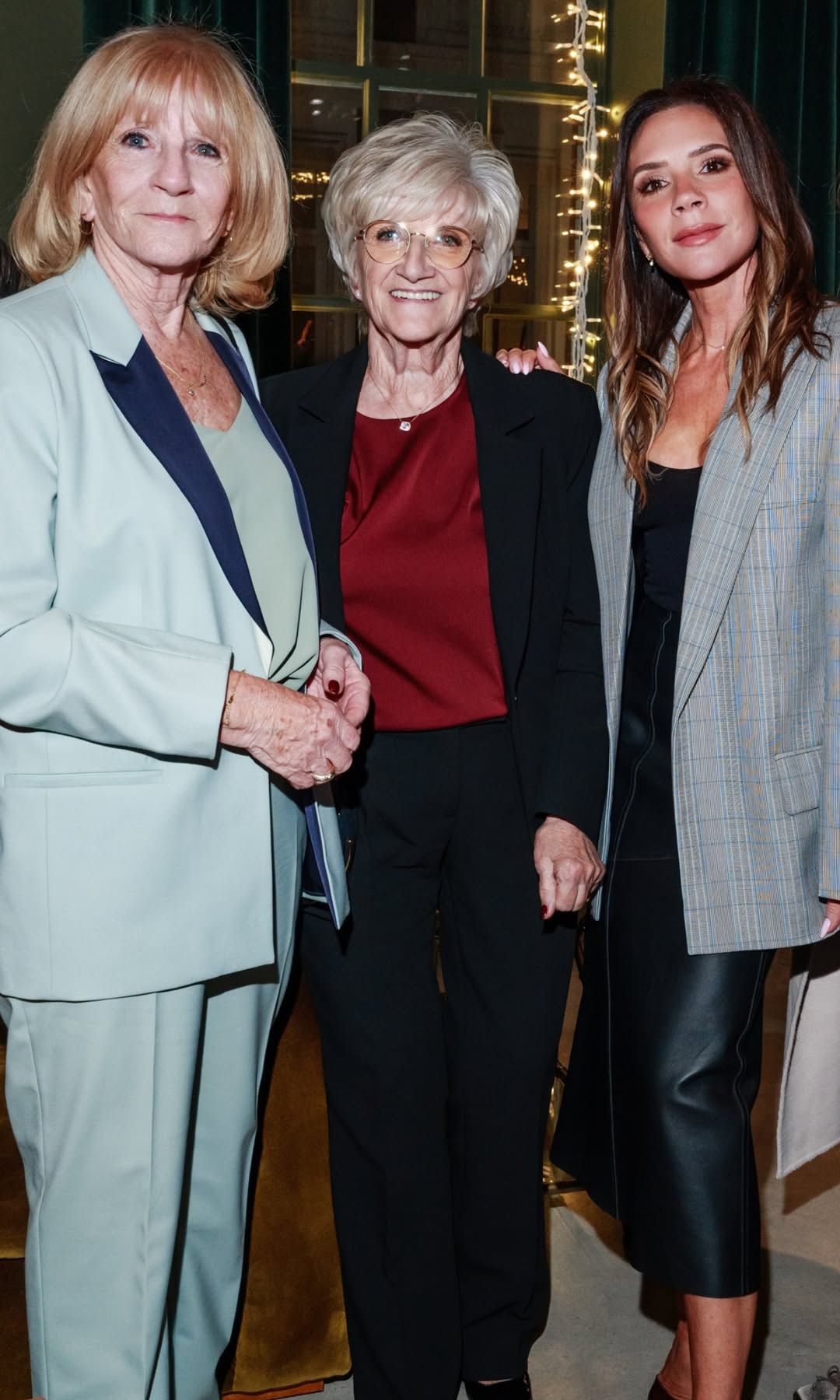Victoria Beckham poses with her mum and mother in law in front of a Christmas tree wearing a checkered blazer and leather midi skirt 
