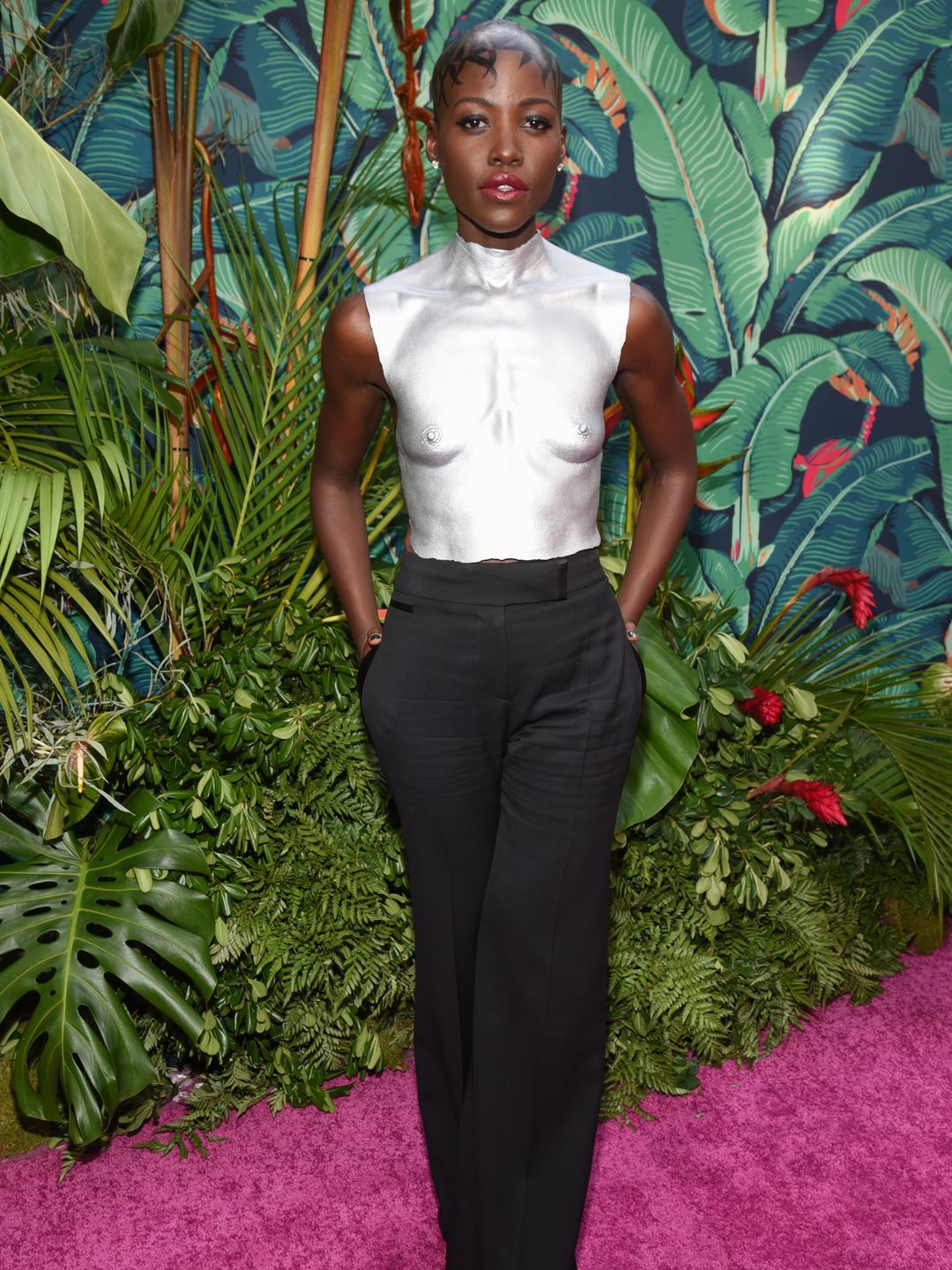 Lupita Nyong'o wearing a silver breastplate and tailored trousers