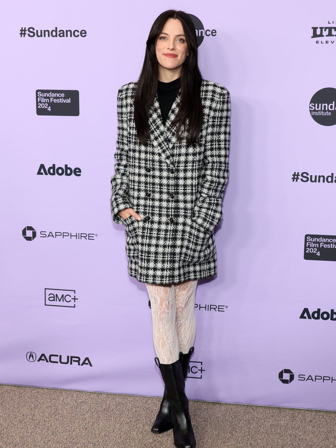 Riley Keough attends the "Sasquatch Sunset" Premiere during the 2024 Sundance Film Festival wearing a checked blazer dress, lace tights and black boots. 