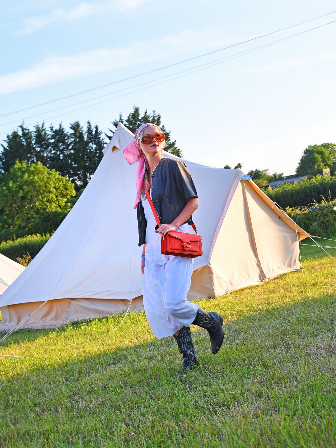 Tilly Clark attended day three of the Glastonbury wearing a white maxi, silk bandana, cowboy boots, and statement red Coach bag. 