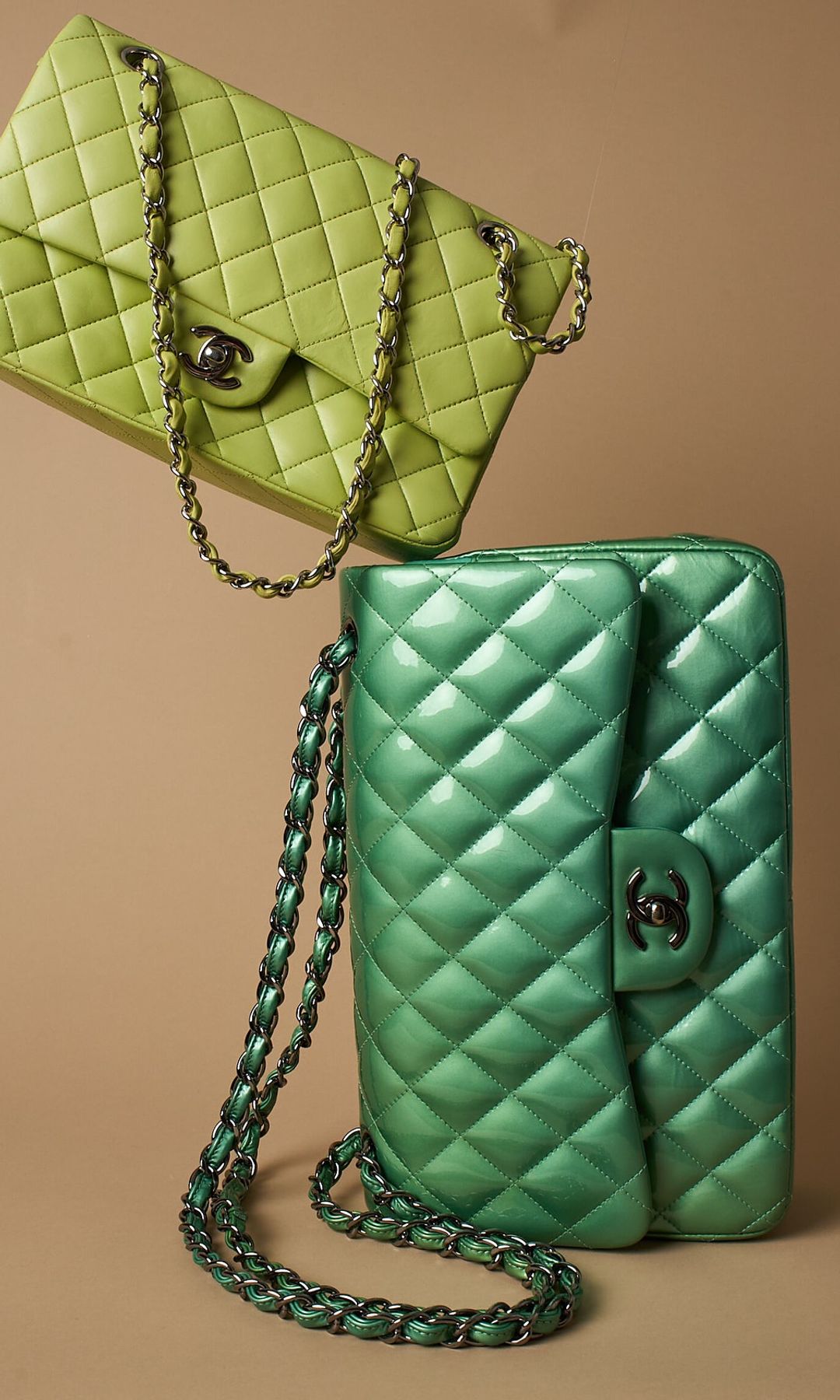 Two green Chanel bags are stacked on-top of each other for a photo in front of a beige background