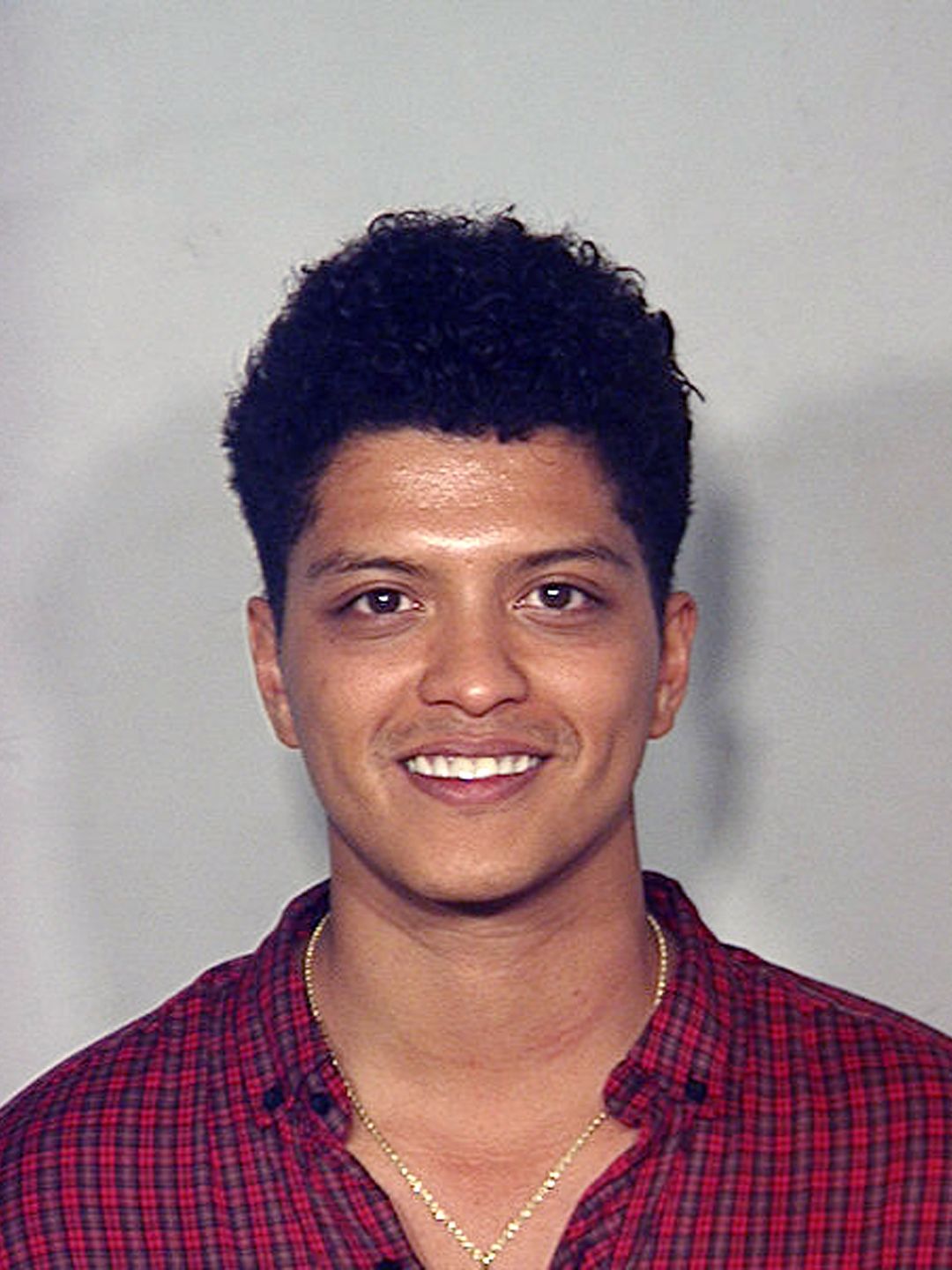 Bruno Mars in a red plaid shirt and necklace for a mugshot