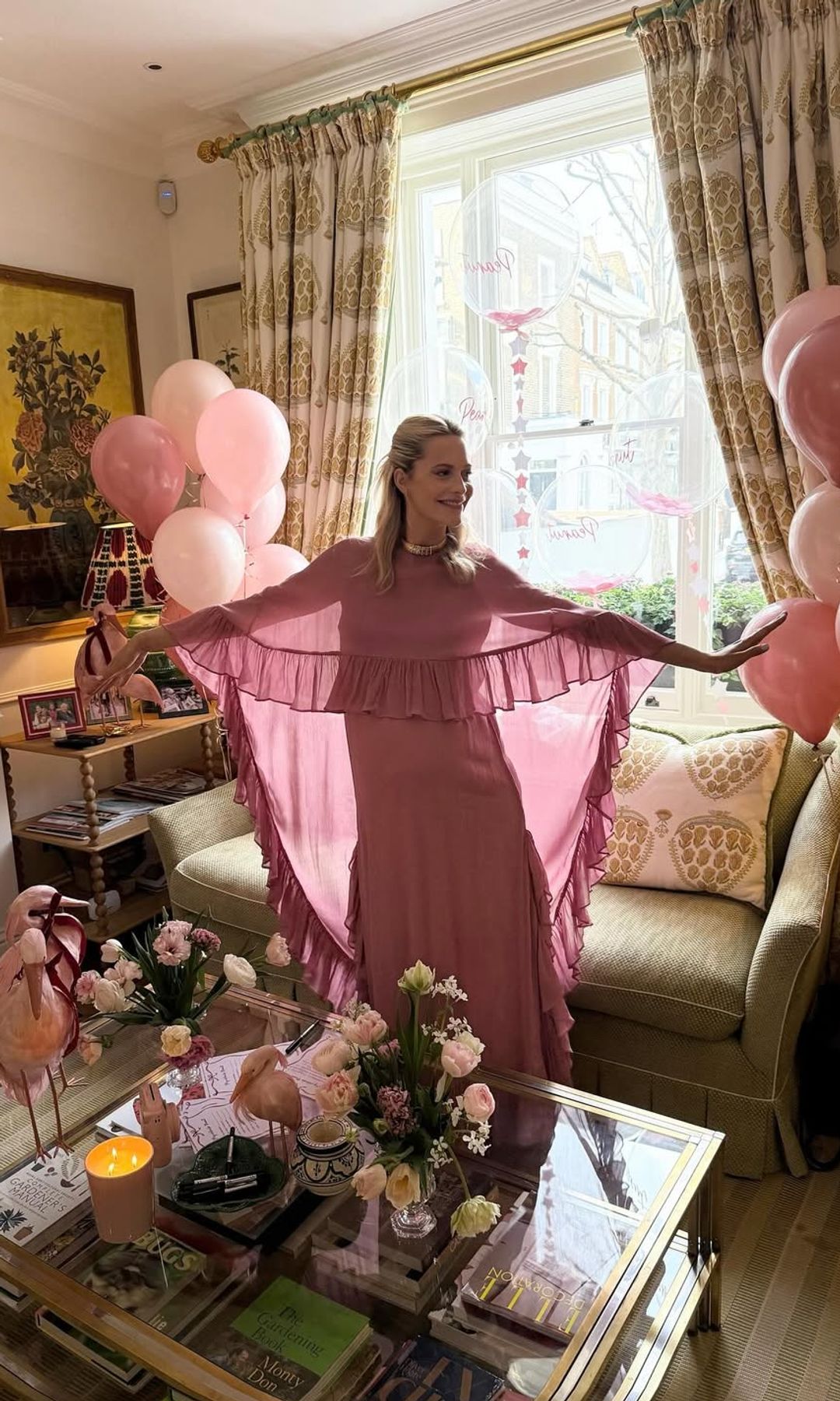Poppy Delevingne showcases the dramatic cape and ruffle detailing of her pink Monsoon dress, glowing with joy during her baby shower at home.