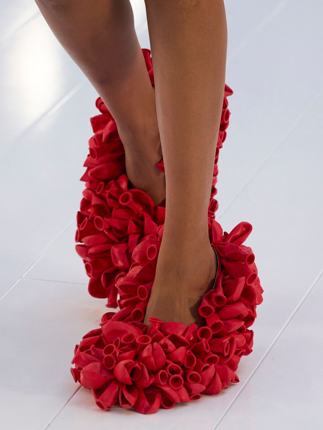 A pair of balloon shoes from the Loewe SS23 Collection, the shoes are bright red and covered in un-inflated balloons.